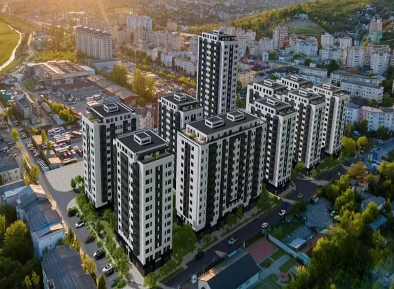 Vizualizare aeriană a ansamblului rezidențial Comat Towers din Iași: mai multe blocuri înalte cu fațade albe și gri închis, într-un cartier urban, în lumina apusului