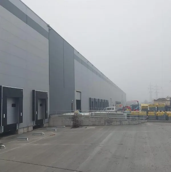 Exteriorul depozitului logistic Dedeman Letea, Bacău: fațadă din panouri gri cu rampe de încărcare, într-o zi cu ceață