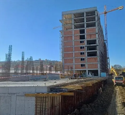 Ansamblul rezidențial Inamstro din Brașov în execuție: structura de beton armat a blocului cu zidărie de cărămidă, macara-turn, armături de așteptare și excavator pe șantier