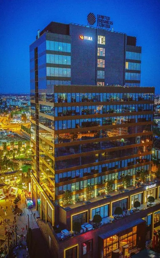 Clădirea United Business Center din Timișoara fotografiată la amurg, cu fațadele luminate și zona pietonală animată de la bază (UBC 3)